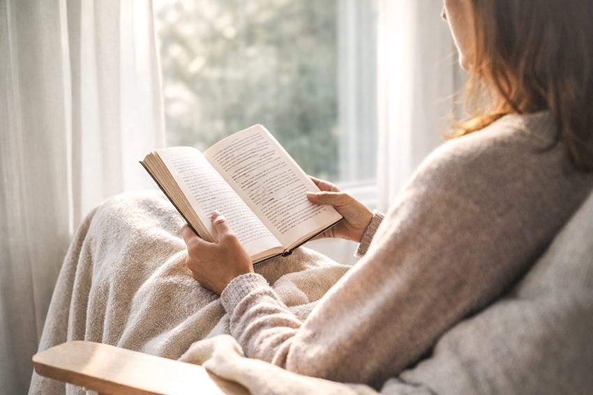 Femme lisant un roman près d’une fenêtre avec lumière naturelle, symbole de reconstruction personnelle grâce à la lecture
